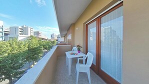 Ein Balkon mit weißem Tisch und Stühlen, einem Blumentopf und Blick auf die Stadt.