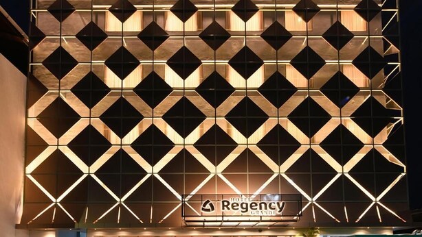 A hotel facade with a geometric pattern, a sign reading 'HOTEL Regency Grande,' and potted plants at the entrance. - Hotel Regency Grande (Thiruvananthapuram)