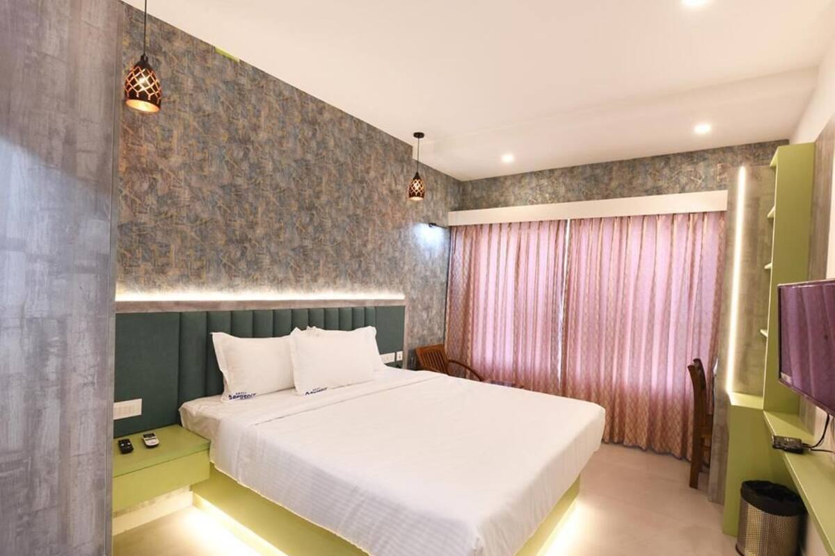 A hotel room with a large bed, bedside tables, a TV, and a curtain.