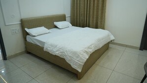 A single bed with a white bedspread and two pillows, a beige headboard, and a curtain on a window. - Hotel Griffin (Anandpur Sahib)
