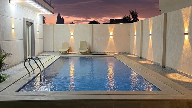 A swimming pool with a metal ladder, two lounge chairs, and wall-mounted lights. - La Dolce Villa with Private Pool (Alexandria Governorate)