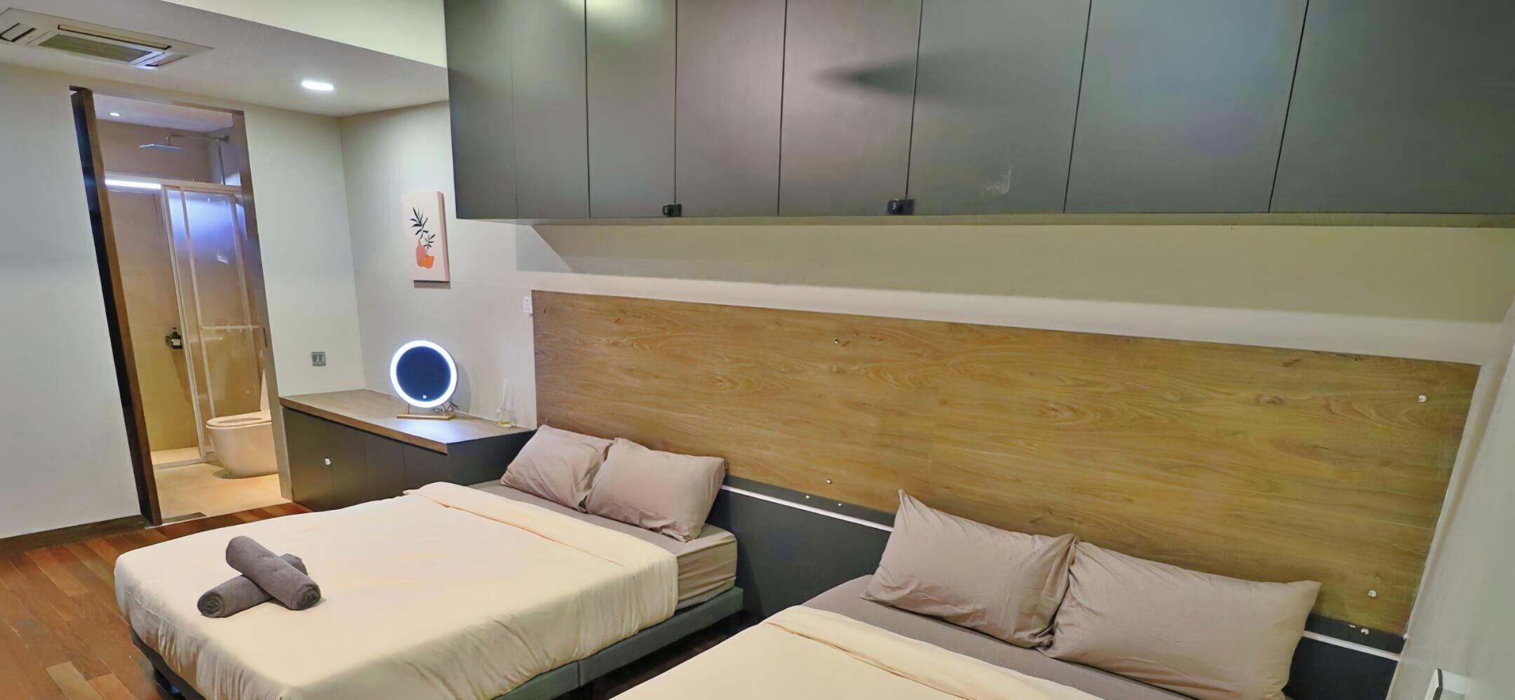 Een moderne hotelkamer met twee bedden, een nachtkastje met lamp, een spiegel en een houten hoofdbord.