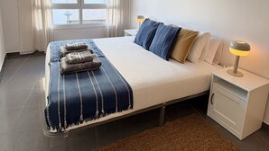 Um quarto moderno com uma cama grande, uma mesa de cabeceira com abajur, uma janela com cortinas e vista para o exterior.