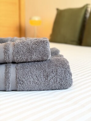 A neatly folded gray towel on a striped bedspread. - Dragos Suites 104 (Arrecife)