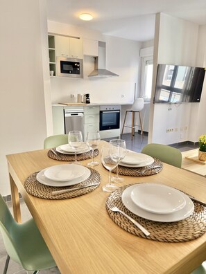 A dining area with a wooden table set for four, surrounded by green chairs. - Dragos Suites 103 (Arrecife)