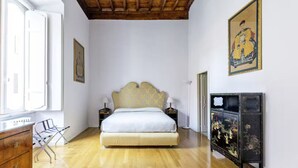 Een slaapkamer met houten vloer, een bed met een bekleder met patroon, nachtkastjes met lampen, een dressoir en een decoratieve kast met bloemwerk.