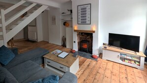 Ett vardagsrum med en öppen spis, en trappa, en soffa, ett soffbord och ett TV-bord.