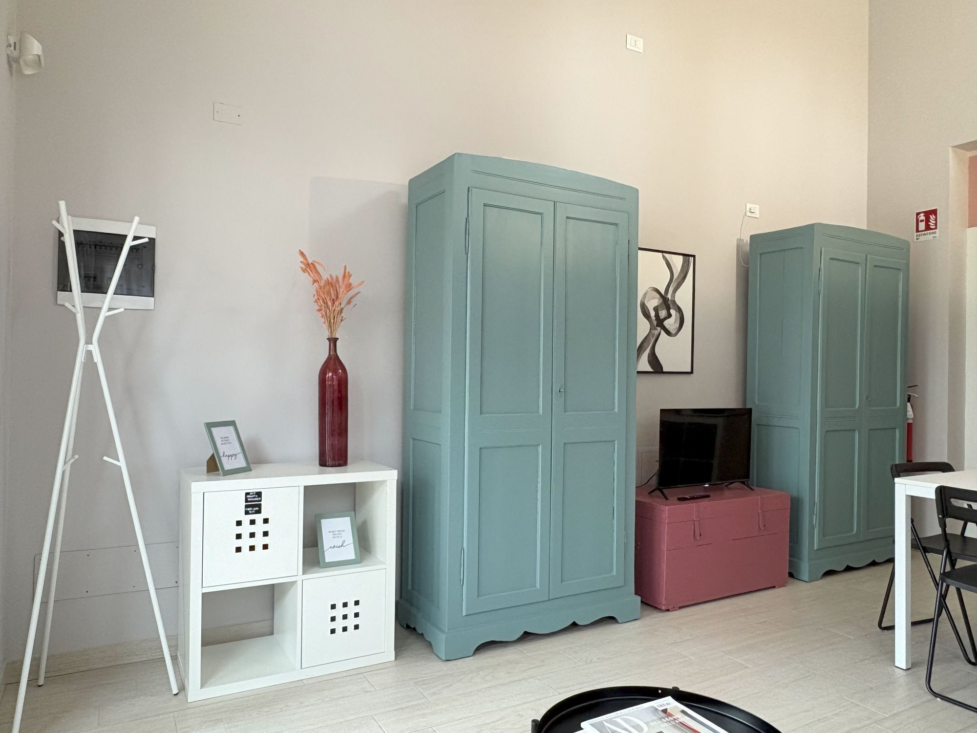 Een kamer met turquoise kasten, een witte tv-meubel, een rode vaas en een lijst met foto op een witte plank.