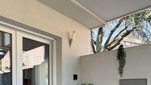 Un balcon avec une porte-fenêtre coulissante, une petite table avec des chaises, une plante en pot et un paillasson.