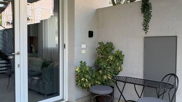 Ein Balkon mit Glastür, einem kleinen Tisch mit Stühlen, einem Blumentopf und einer Fußmatte.