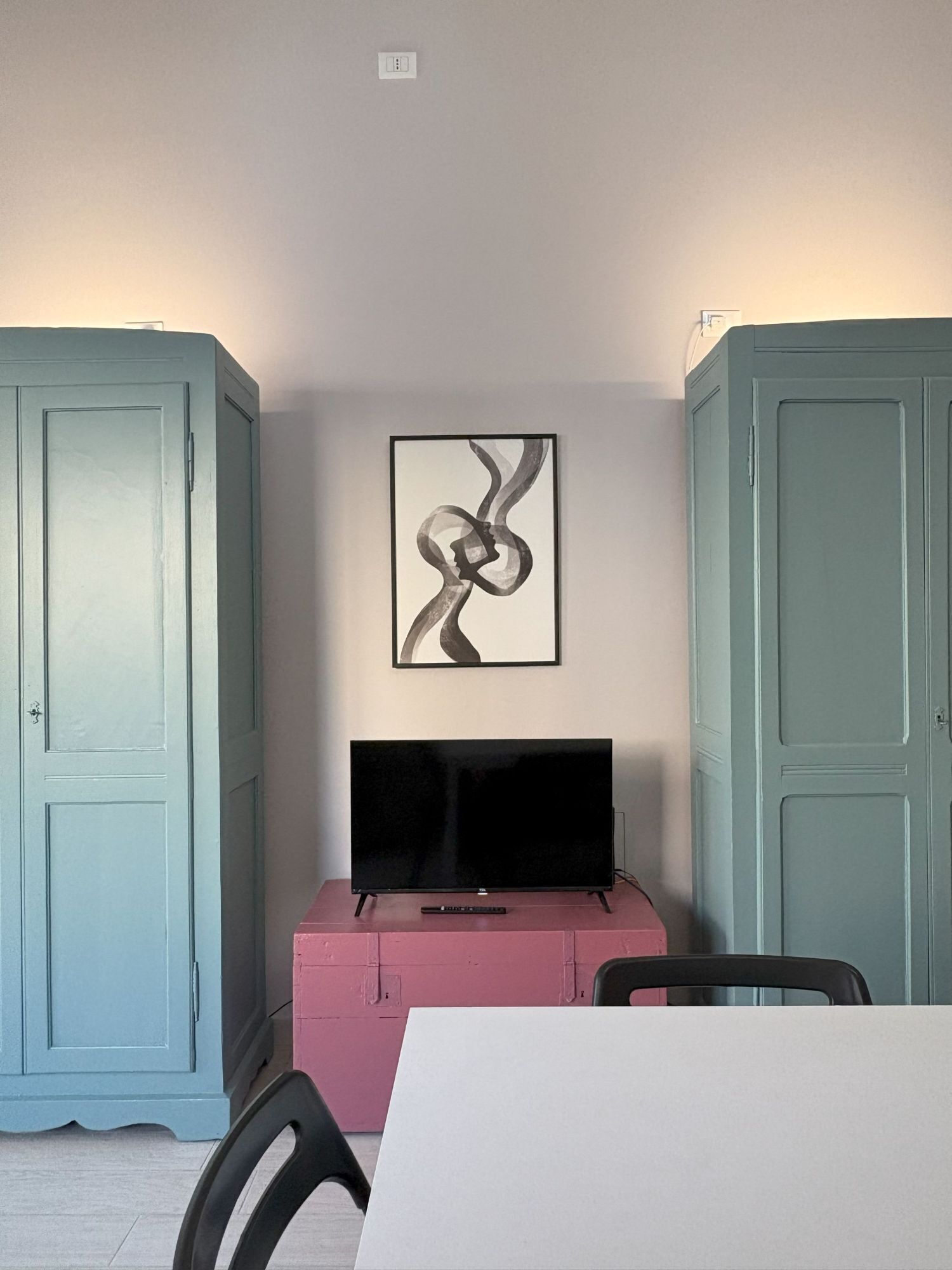 Ein Zimmer mit einem Flachbildfernseher auf einer rosafarbenen Kommode, einem gerahmten abstrakten Kunstwerk an der Wand und hellblauen Schränken.
