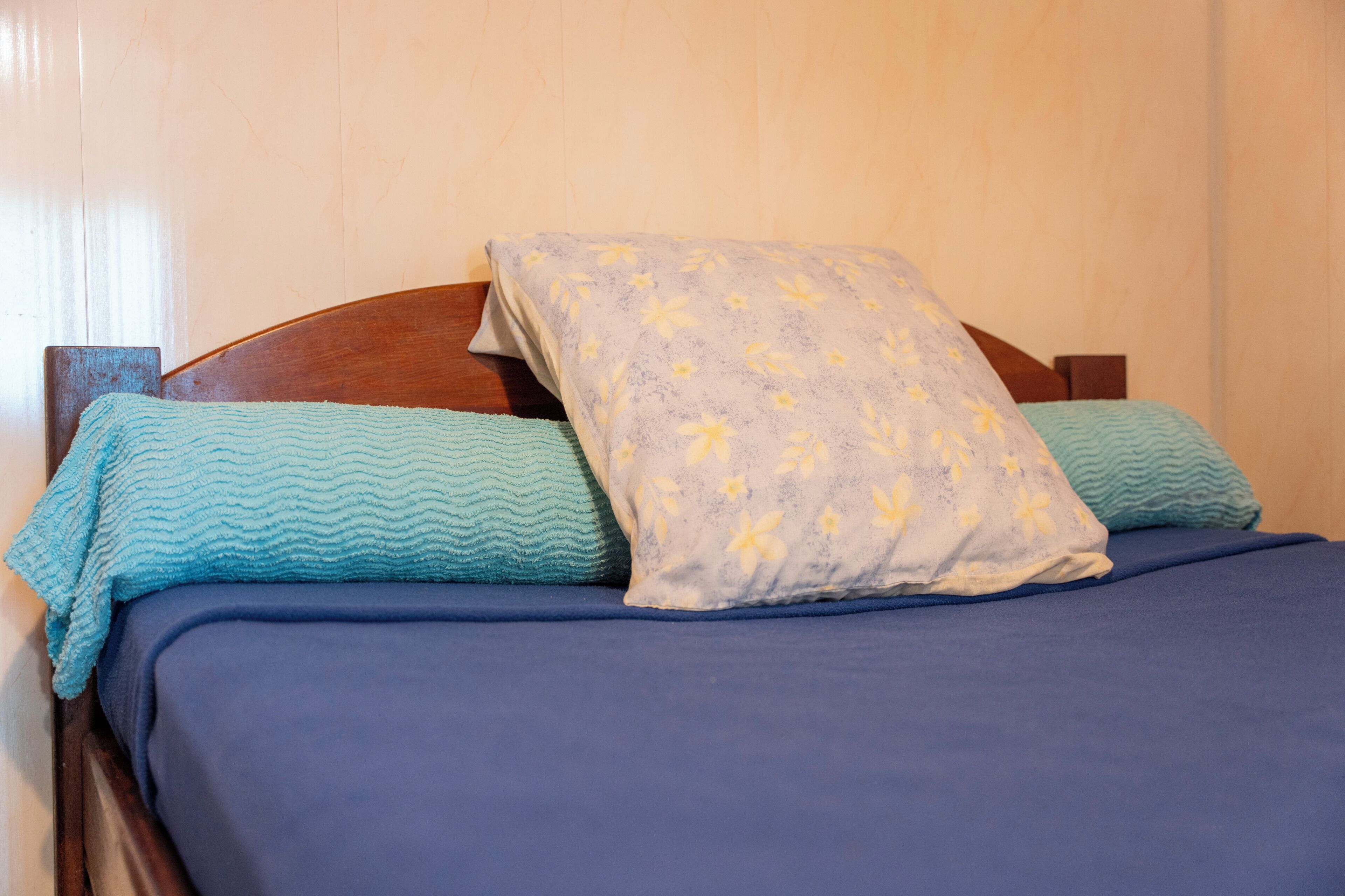 Een bed met een houten hoofdbord, blauw beddengoed en twee kussens met bloemenmotieven.
