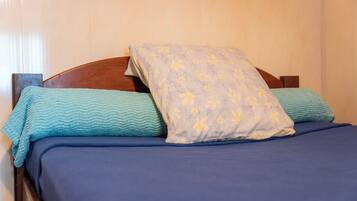 Een bed met een houten hoofdbord, blauw beddengoed en twee kussens met bloemenmotieven.