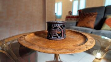 Una mesa redonda de madera con cubierta de vidrio, una taza de madera decorativa y un sofá con cojines al fondo.