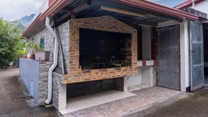 A brick-built outdoor kitchen with a metal roof, a stone wall, and a tiled floor. - La Kaz Montagne Authentique, 6 pers. Mountain view, with Creole garden (Cilaos)