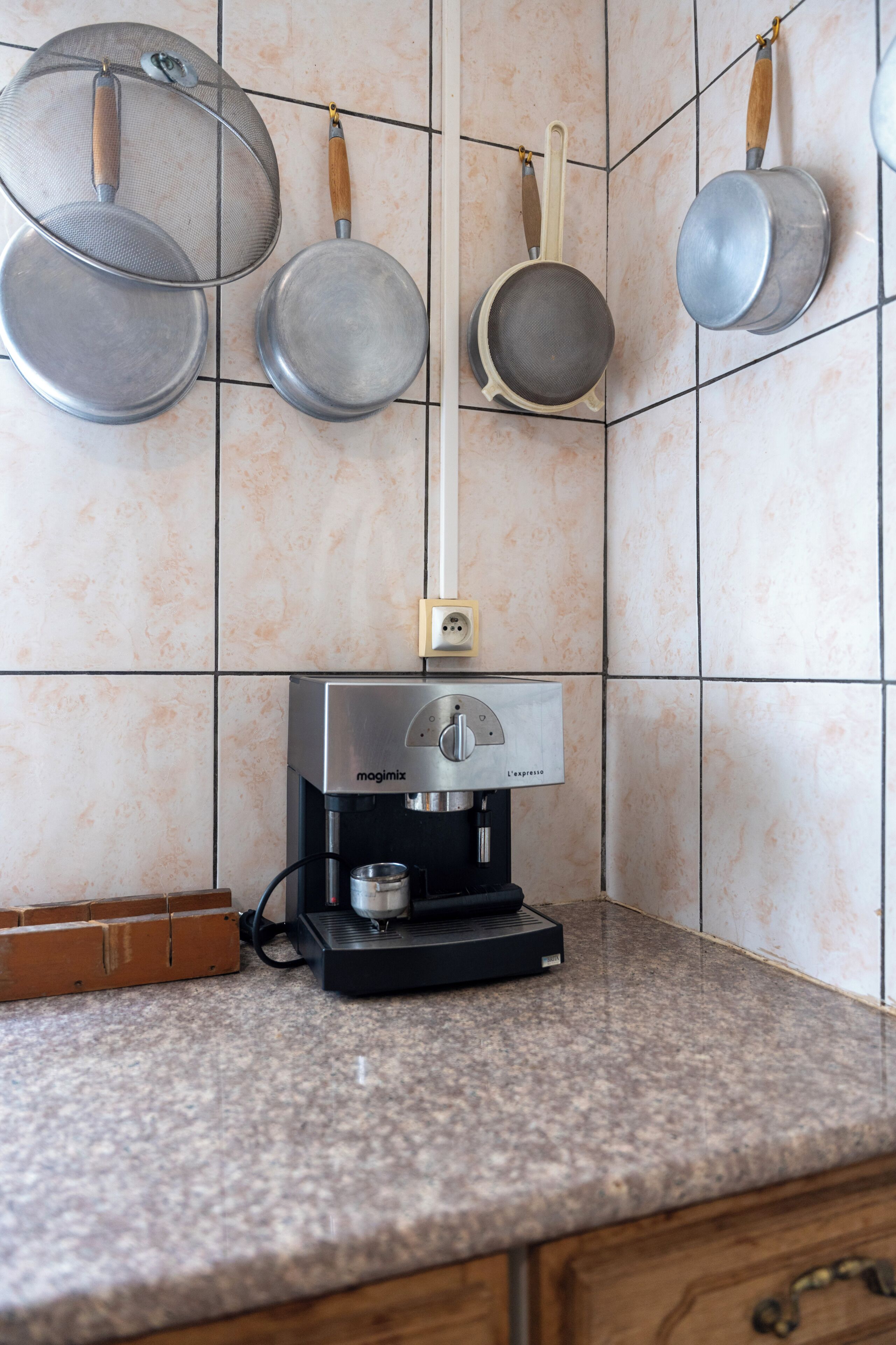 Een keuken met een koffieapparaat, hangende pannen en een betegelde achterwand.