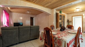 A dining area with a table set for four, wooden chairs, a sofa, a television, and a wooden ceiling. - La Kaz Montagne Authentique, 6 pers. Mountain view, with Creole garden (Cilaos)