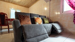 A modern living room with a sofa, a wooden chair, and a window with curtains. - La Kaz Montagne Authentique, 6 pers. Mountain view, with Creole garden (Cilaos)