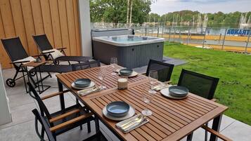 Un área de comedor al aire libre con mesa de madera dispuesta para dos, un jacuzzi y sillones de descanso.