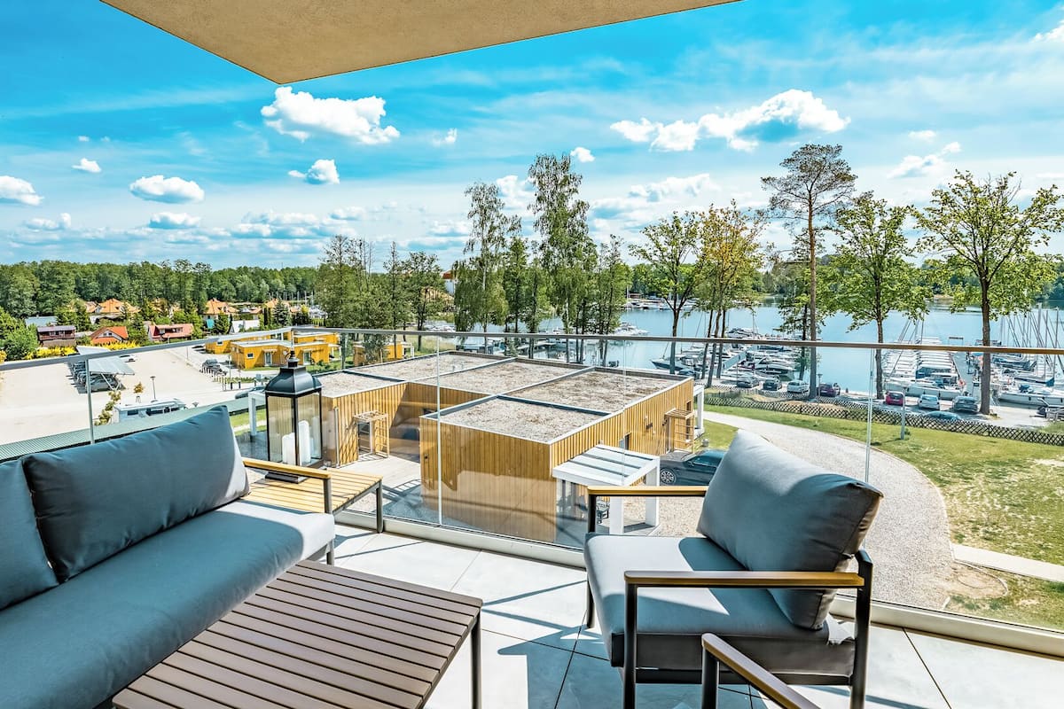 A modern outdoor terrace with a view of a marina and boats, furnished with a sofa, chairs, and a table.