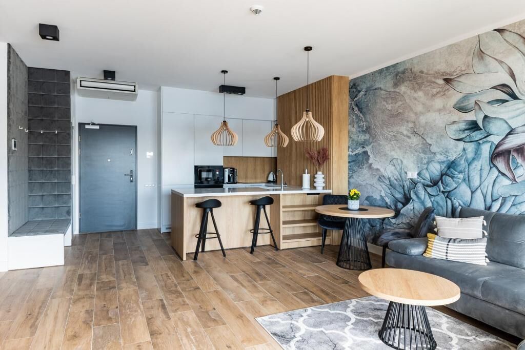 A modern kitchen with a central island, bar stools, pendant lights, and a dining area with a round table and sofa.
