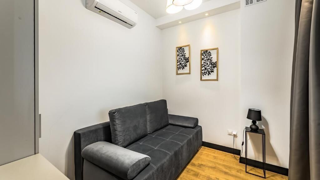 Une pièce moderne avec un canapé gris, une petite table avec une lampe et deux œuvres d’art accrochées au mur.