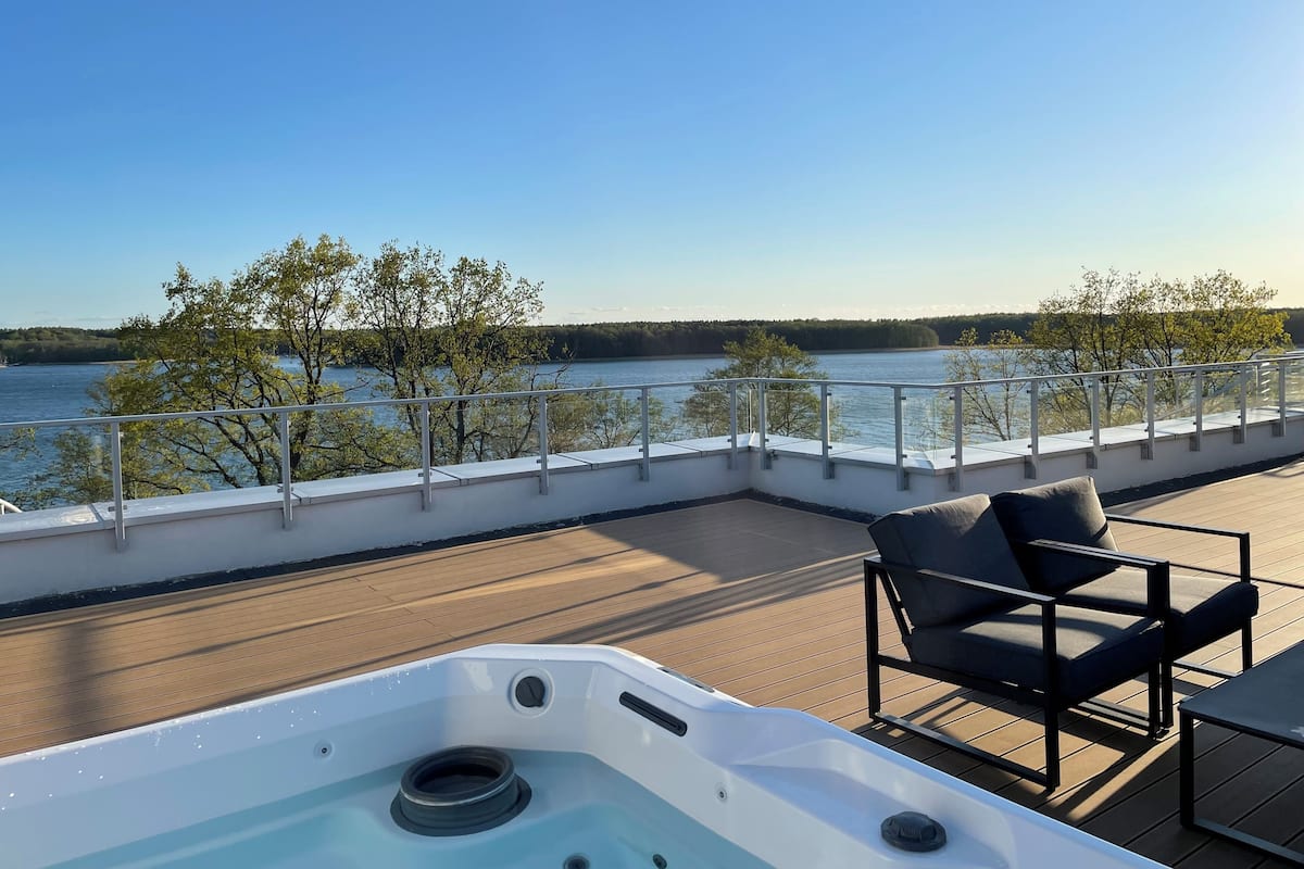 A deck with a hot tub, chairs, and a view of a lake.