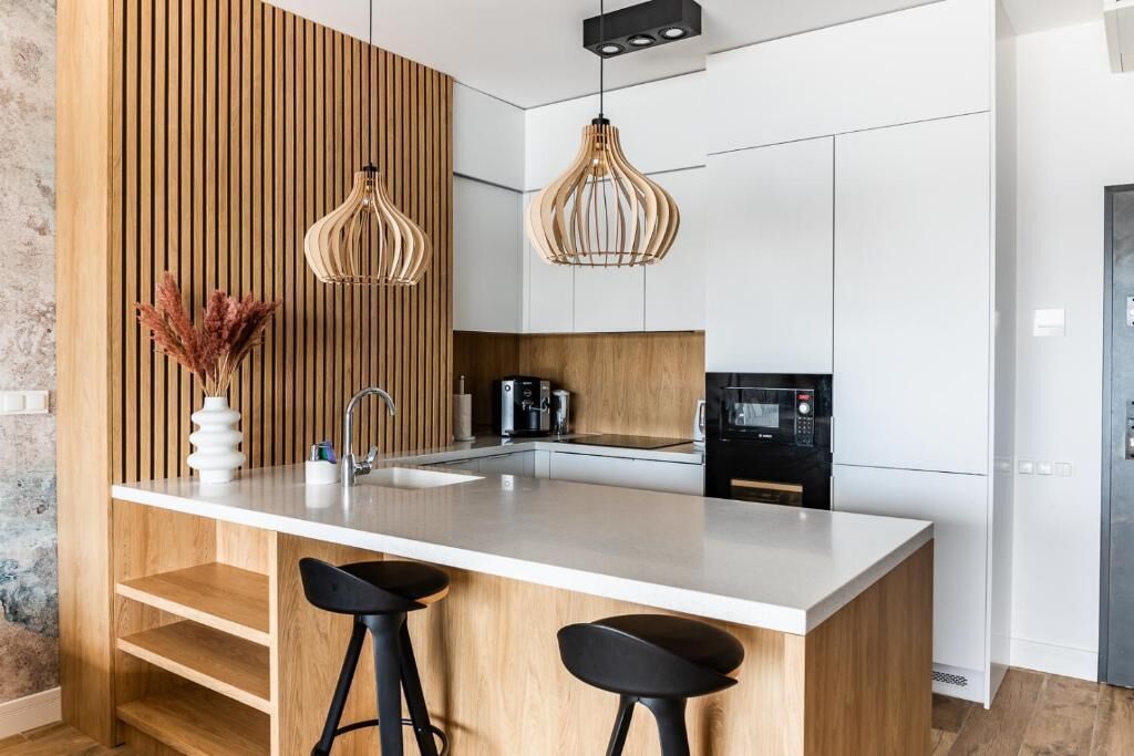 A modern kitchen with a central island, bar stools, wooden paneling, and pendant lighting.
