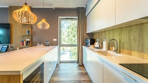 A modern kitchen with a central island, pendant lights, a view through the window, and a 'Smile' sign on the wall.