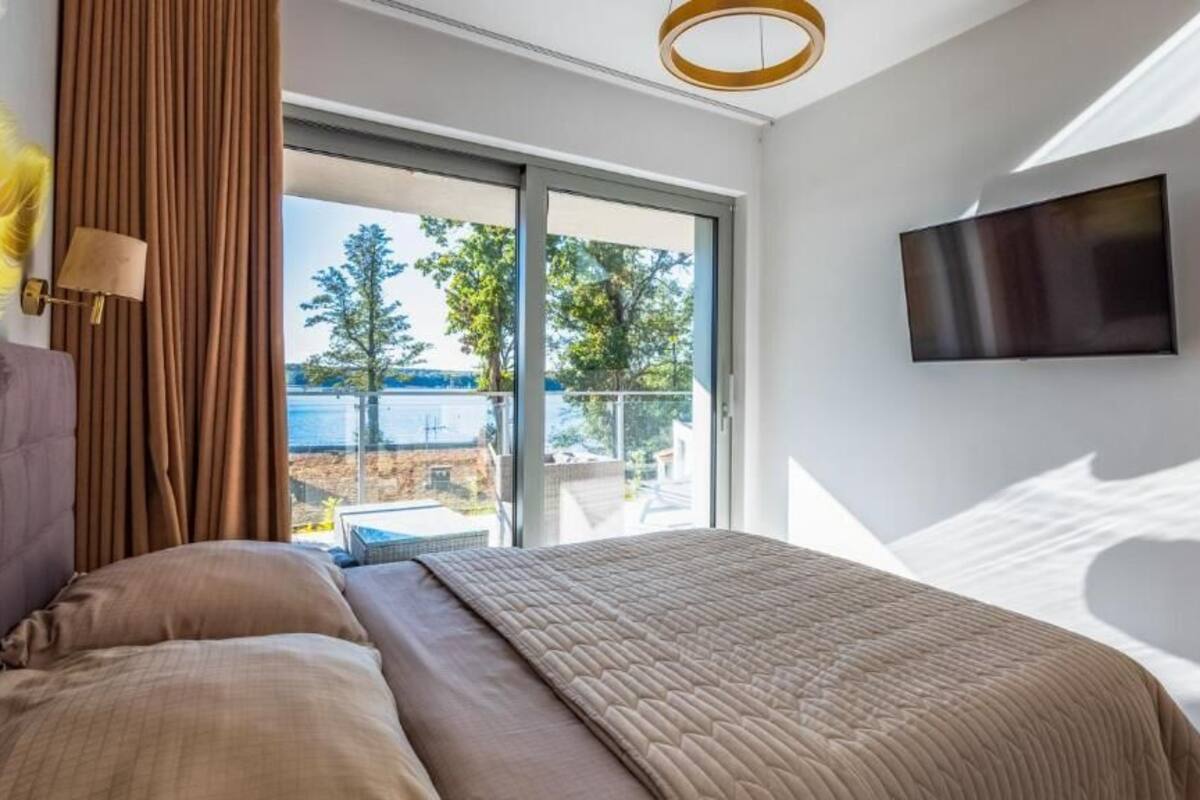 A bedroom with a large bed, a TV mounted on the wall, and a sliding glass door leading to an outdoor area.