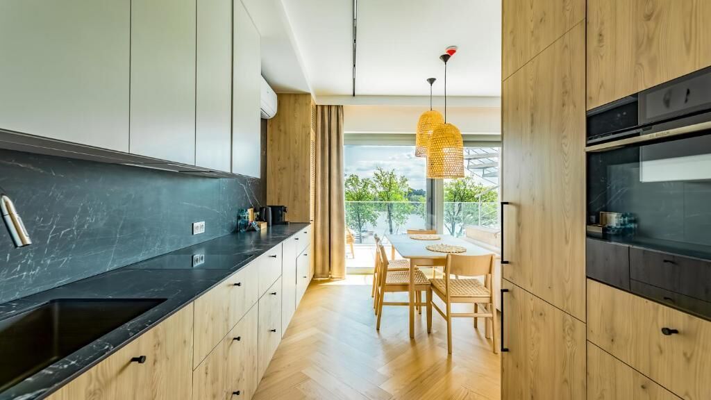 Una cocina moderna con armarios de madera, encimera negra y un comedor con mesa y sillas.