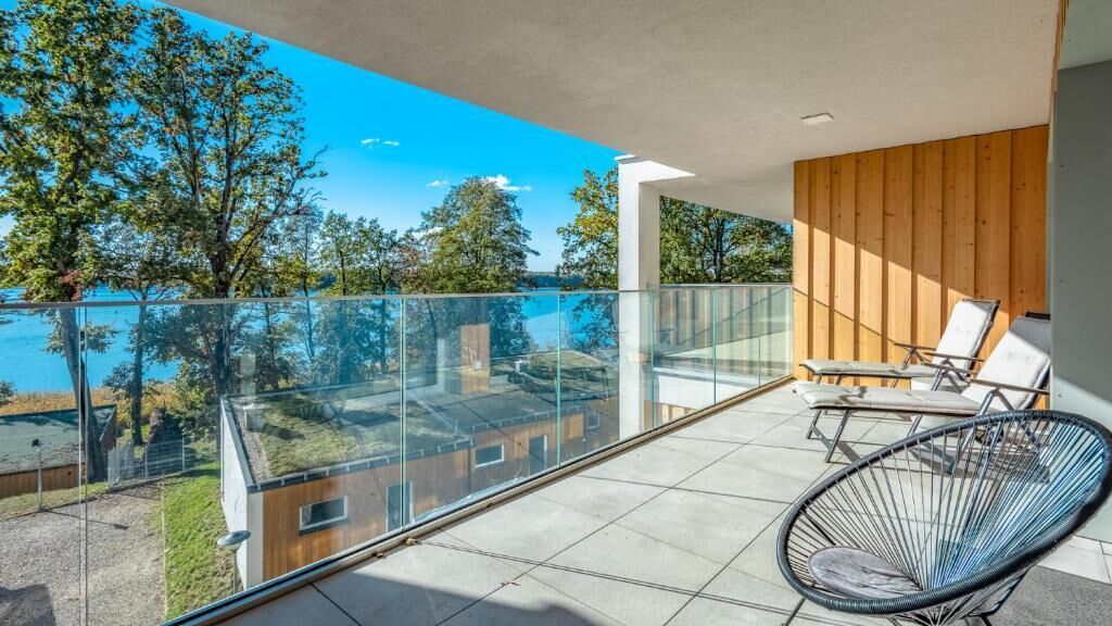 Een balkon met glazen hekwerk, een stoel en uitzicht op bomen en gebouwen.
