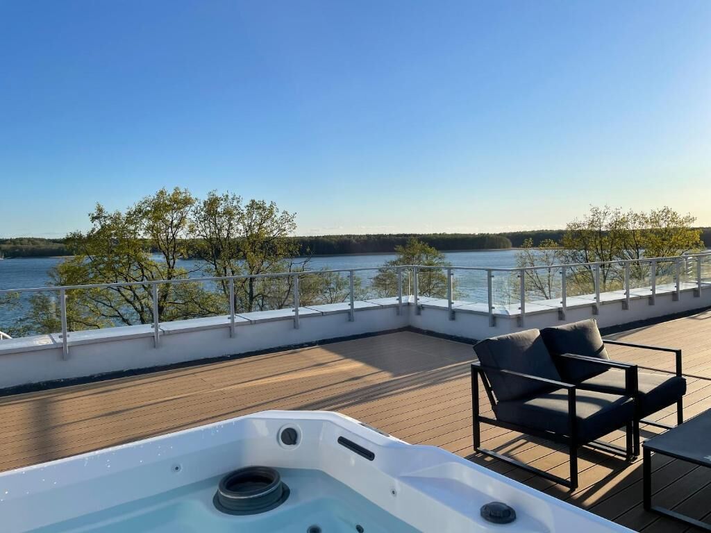 Una terraza con jacuzzi, sillas y vistas a un lago.