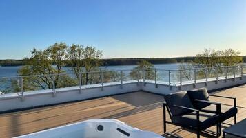 Una terraza con jacuzzi, sillas y vistas a un lago.