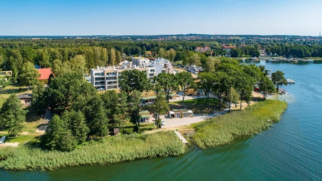 An aerial view of a lakeside property with a modern building, surrounded by dense trees and a calm lake.
