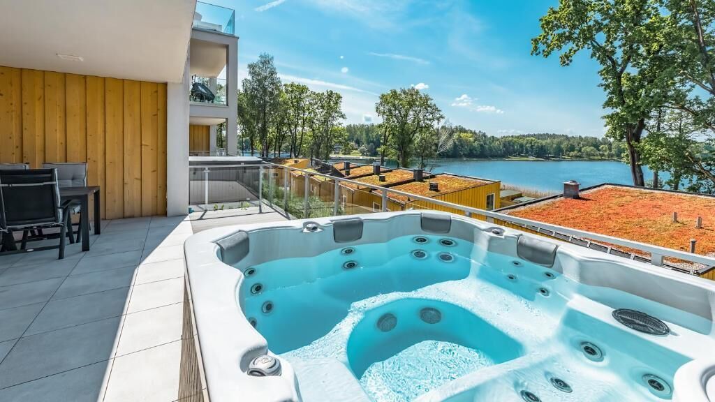 Un bain à remous extérieur moderne offrant une vue dégagée sur un lac et des arbres.