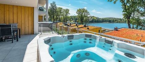 Un bain à remous extérieur moderne offrant une vue dégagée sur un lac et des arbres.
