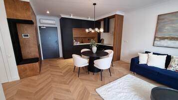 A modern living room with a dining area, wooden flooring, a blue sofa, and a white rug.