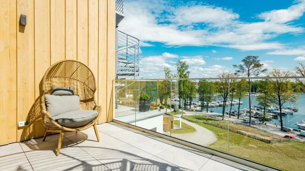 Un balcon avec un fauteuil en osier, une balustrade en verre et une vue sur une marina remplie de bateaux.