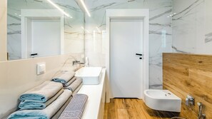 Un bagno moderno con una parete in marmo, un mobile bagno in legno, un lavandino bianco, un bidet e uno specchio.
