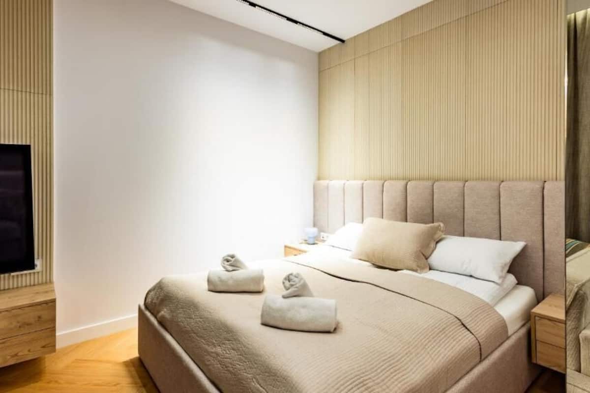 A modern hotel room with a large bed, a flat-screen TV, a wooden dresser, and a sofa.