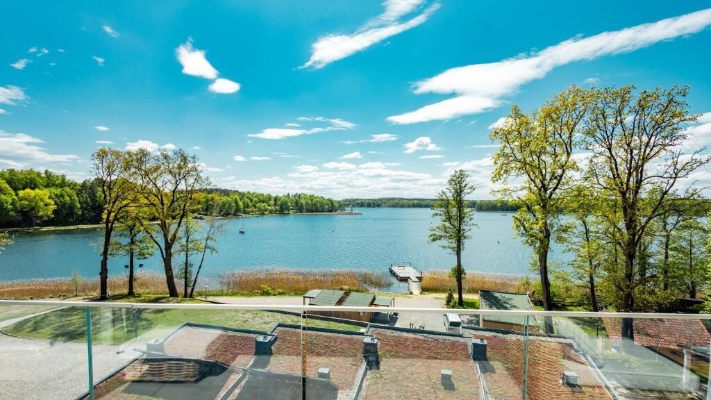 A lakeside view from a high vantage point, featuring a clear sky, a calm lake, and a parking area with a glass railing.