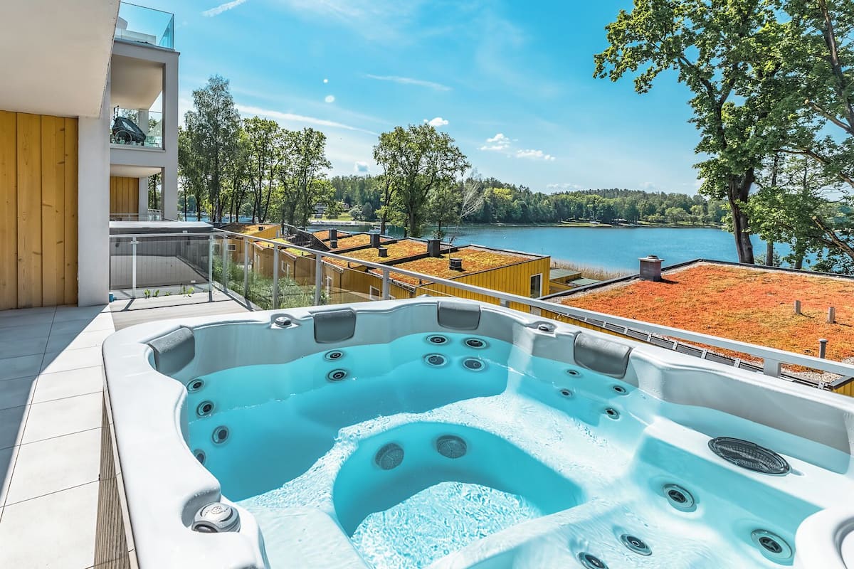 A hot tub on a balcony with a view of a lake and trees.