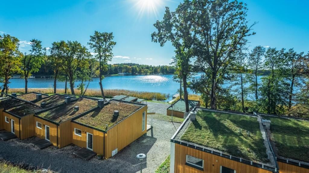 Una cabana al costat d'un llac amb teulada d'herba, un camí de grava i vista cap al llac.