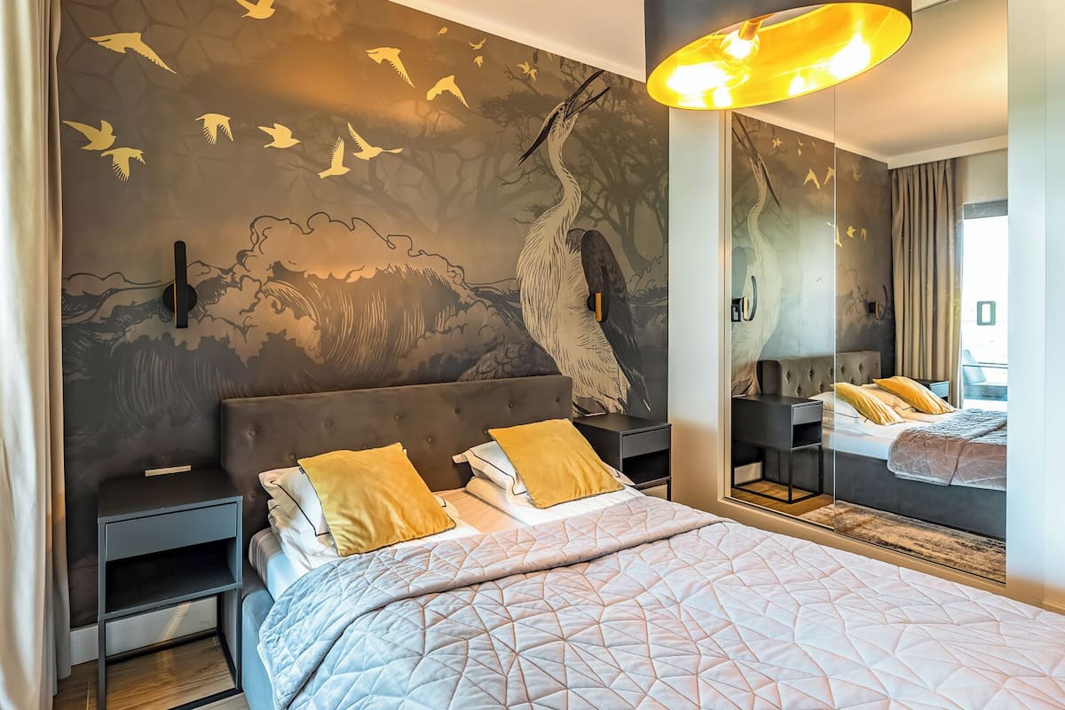 A modern bedroom with a large bed, nightstands, a mirror, and a wall mural.