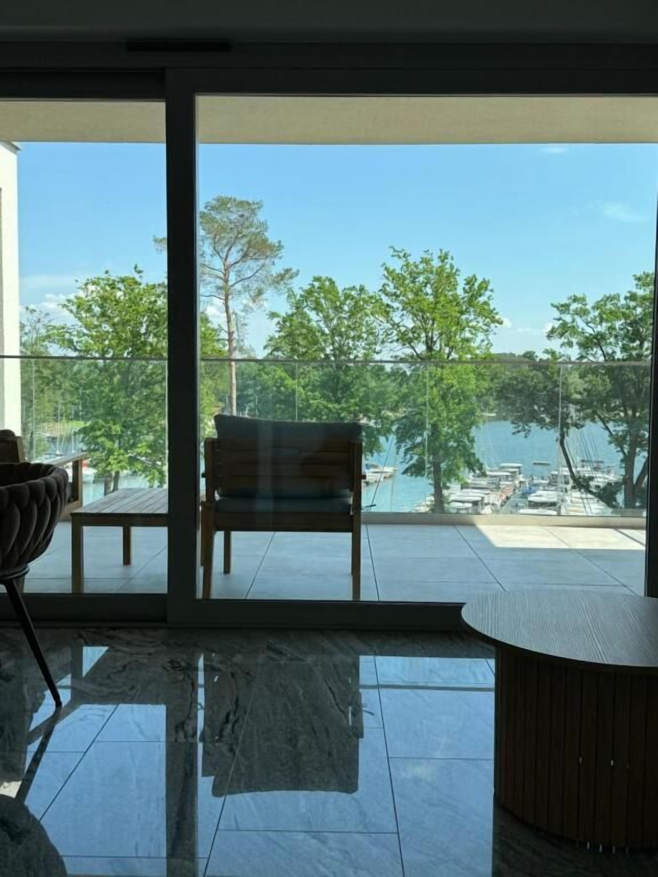 A modern room with a large glass door leading to a balcony with a view of a lake and boats.
