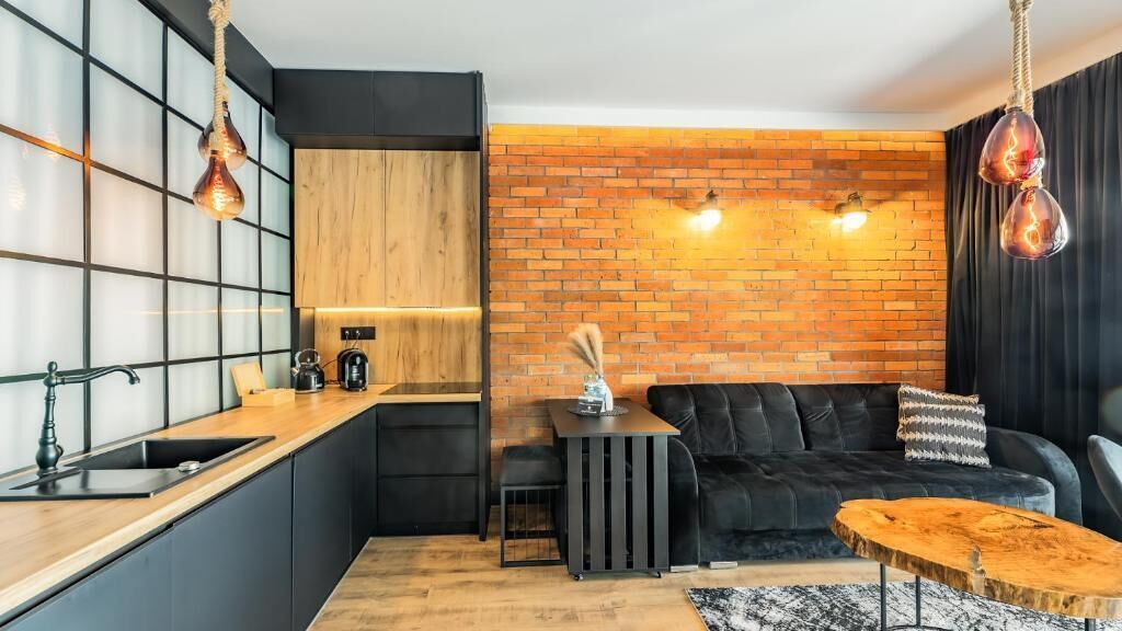 A modern kitchen with a black countertop, wooden cabinets, and a brick wall.