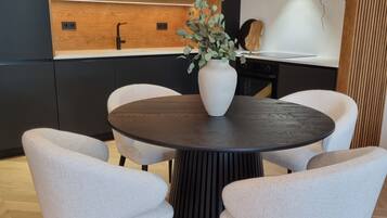 Un comedor moderno con una mesa redonda, cuatro sillas, un jarrón con follaje, una lámpara esférica original y una pared de acento de madera.