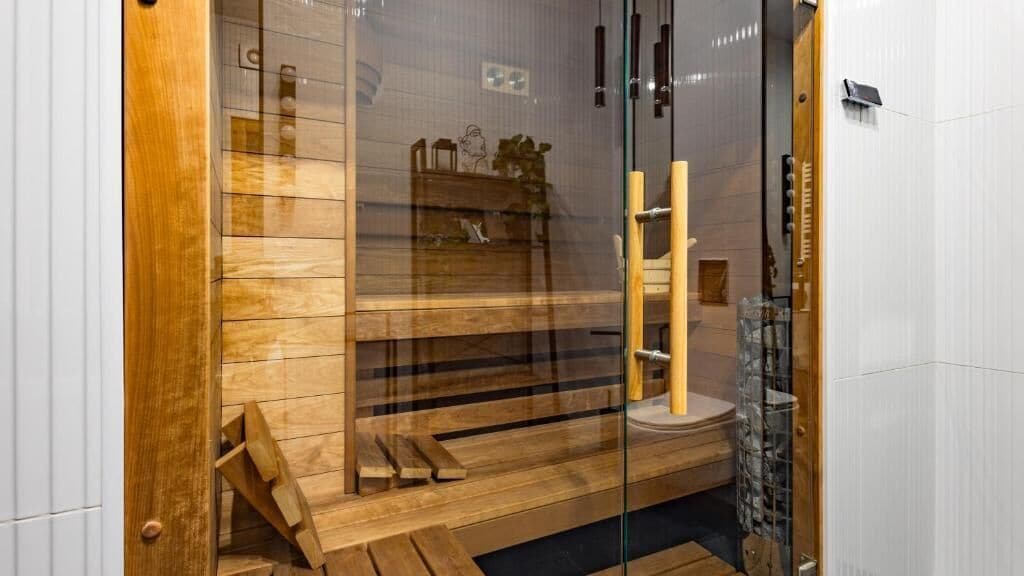 A sauna with wooden benches, a glass door, and a wooden ladder.