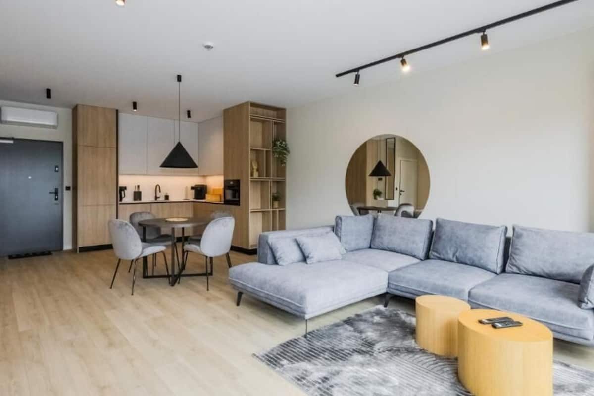 A modern living room with a grey sectional sofa, a round coffee table, and a dining area with a small table and chairs.